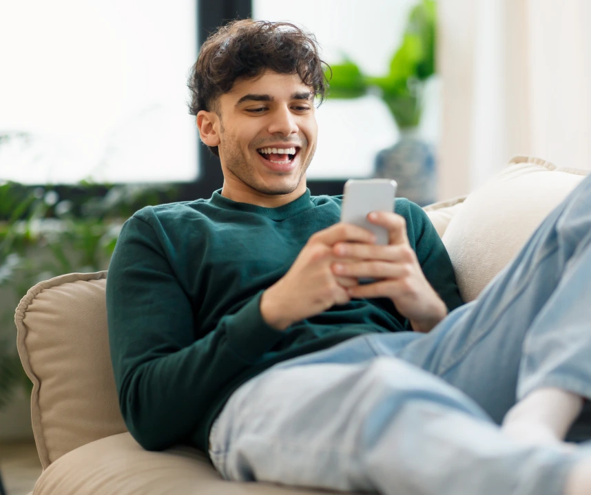 Man smiling at his phone on the sofa – online psychiatry in Bend, OR